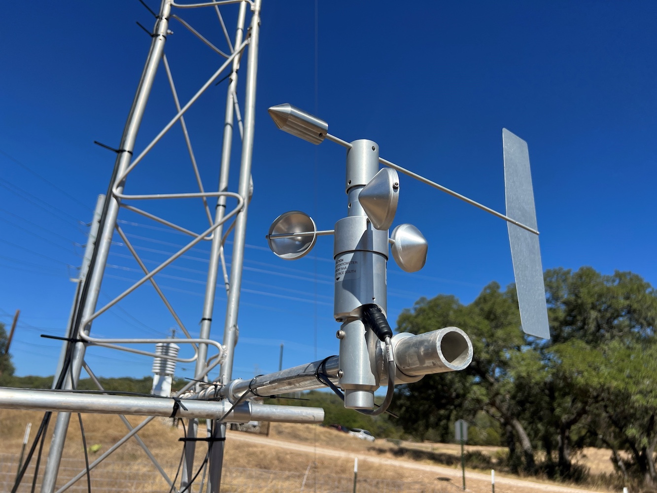 Weather station wind sensor against a clear blue sky in a rural setting