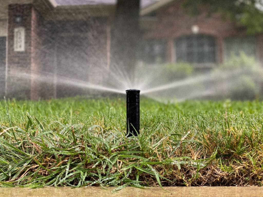 Lawn sprinkler watering green grass in a garden setting near a brick house