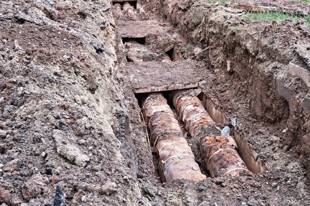 underground-pipe-trench-repair-construction Old clay pipes exposed in a dirt trench during construction work (dismantling)
