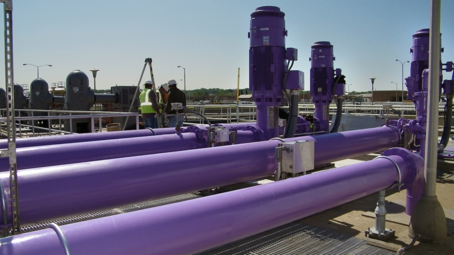Purple industrial pipes and machinery at a water treatment facility under clear blue sky