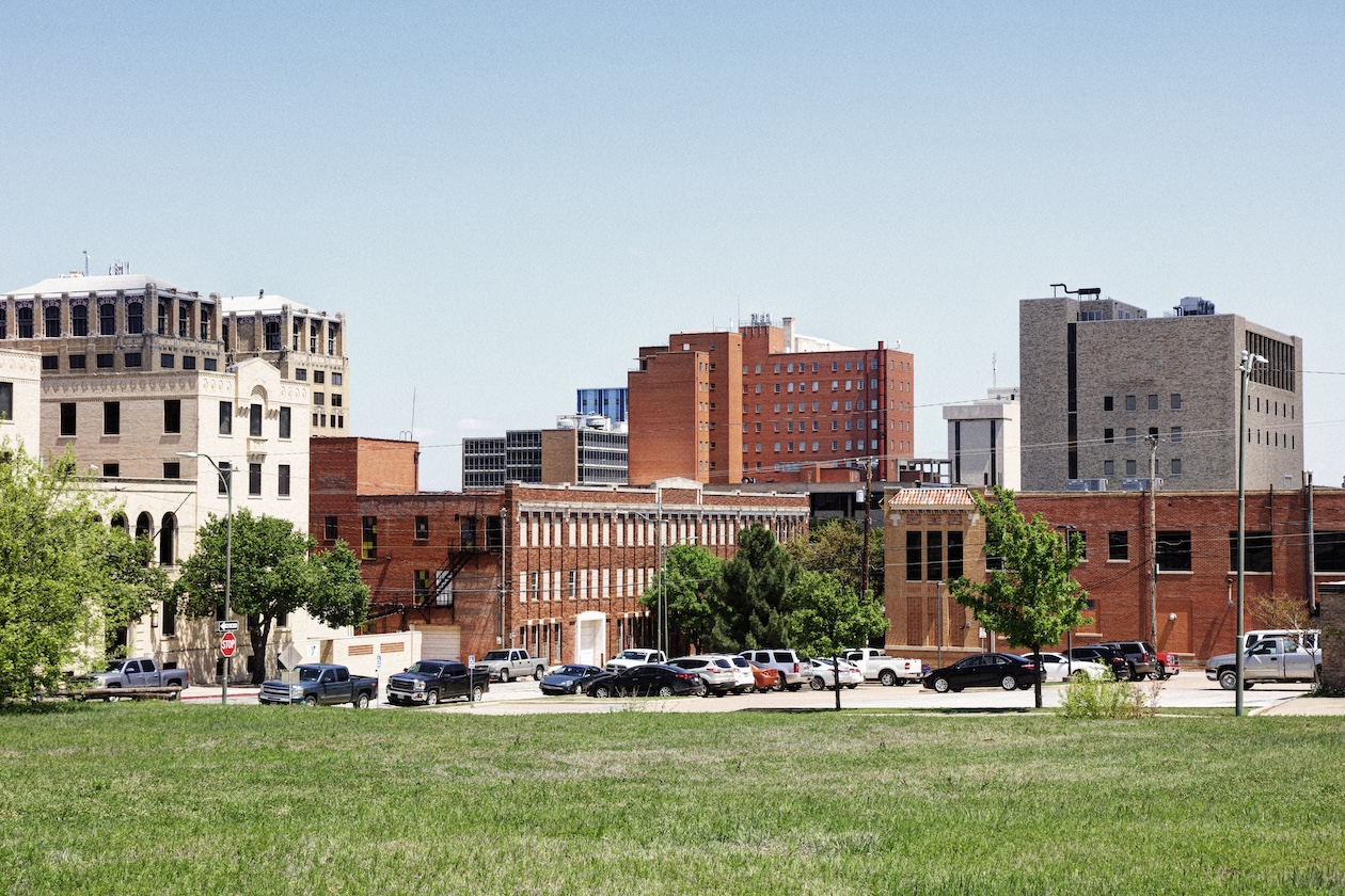City skyline with historic buildings and parked cars viewed from a green park area