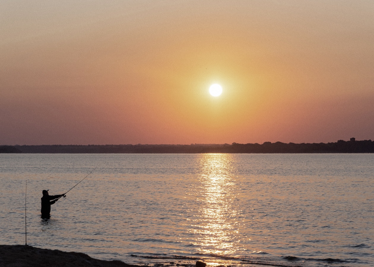 Pescador en silueta ante una serena puesta de sol sobre aguas oceánicas en calma
