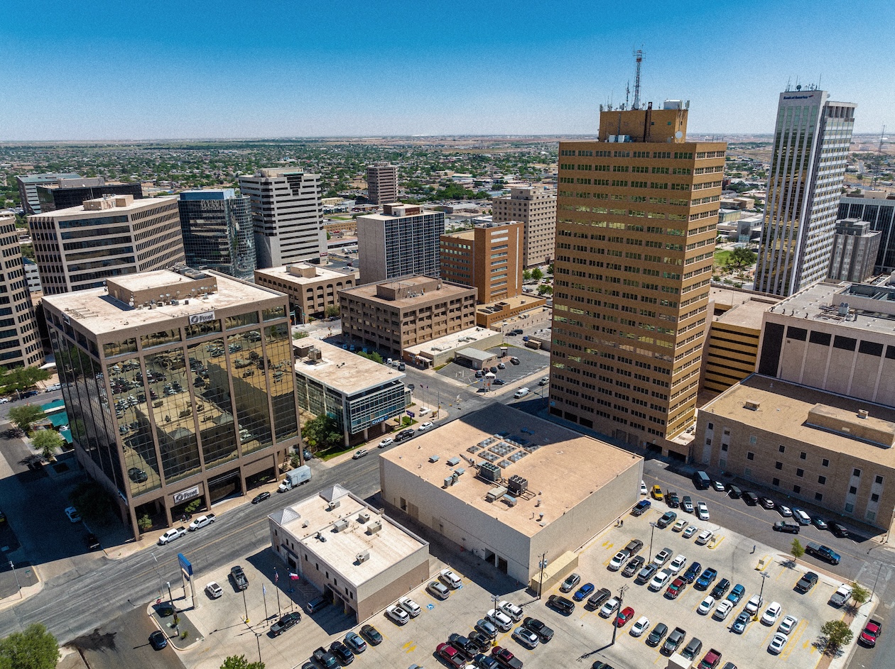 Aerial view of a bustling cityscape with tall office buildings under a clear blue sky
