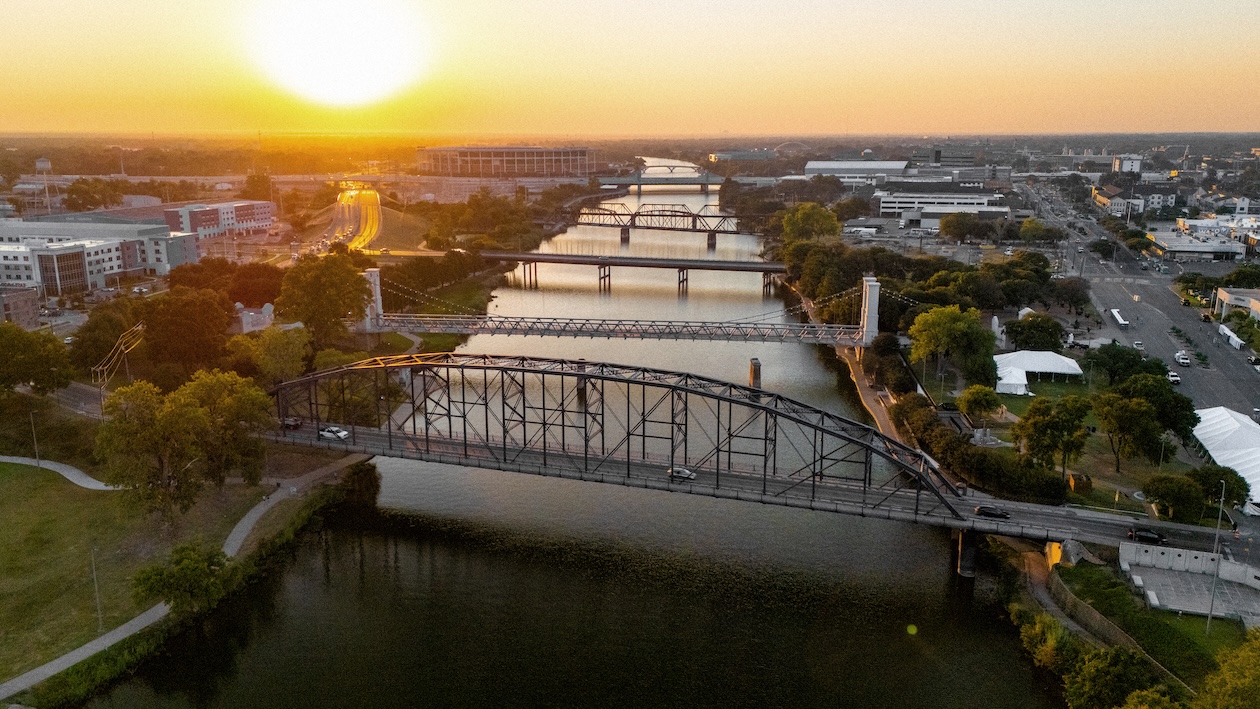 Sunset view of a cityscape with bridges over a river and surrounding greenery