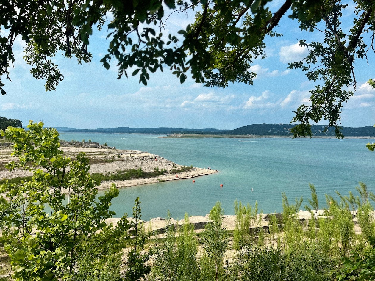 Scenic lake view with clear blue water and lush green trees under a bright sky