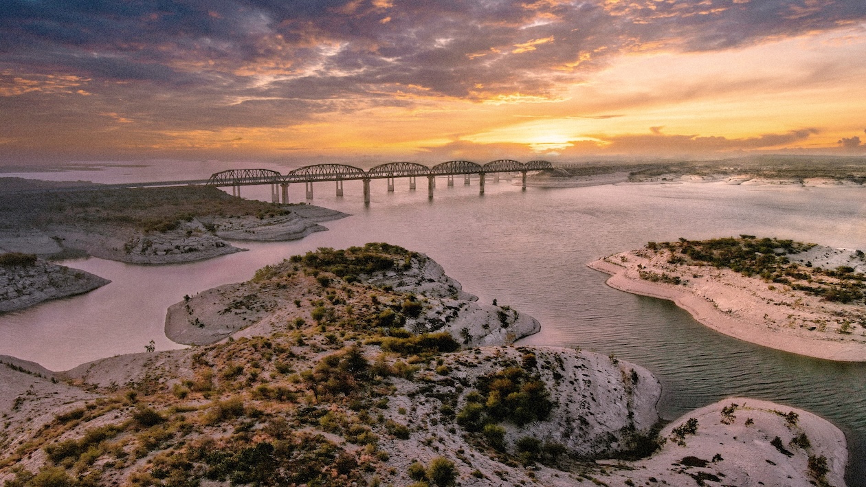 Scenic sunset over a winding river bridge with sandy islands and colorful sky